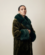 Manteau long femme en fausse fourrure vegan vert profond, poils courts brillants, col et poignets oversize contrastés, coupe droite structurée, confection artisanale parisienne MQV Paris.